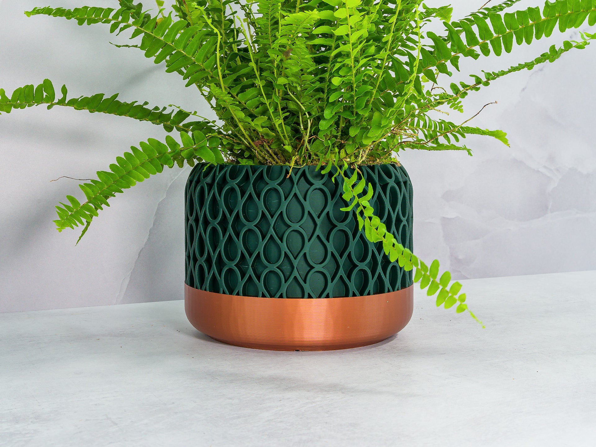 Angled with Fern: "Angled view of DROPLET planter with copper base and forest pattern, showcasing a fern plant."
