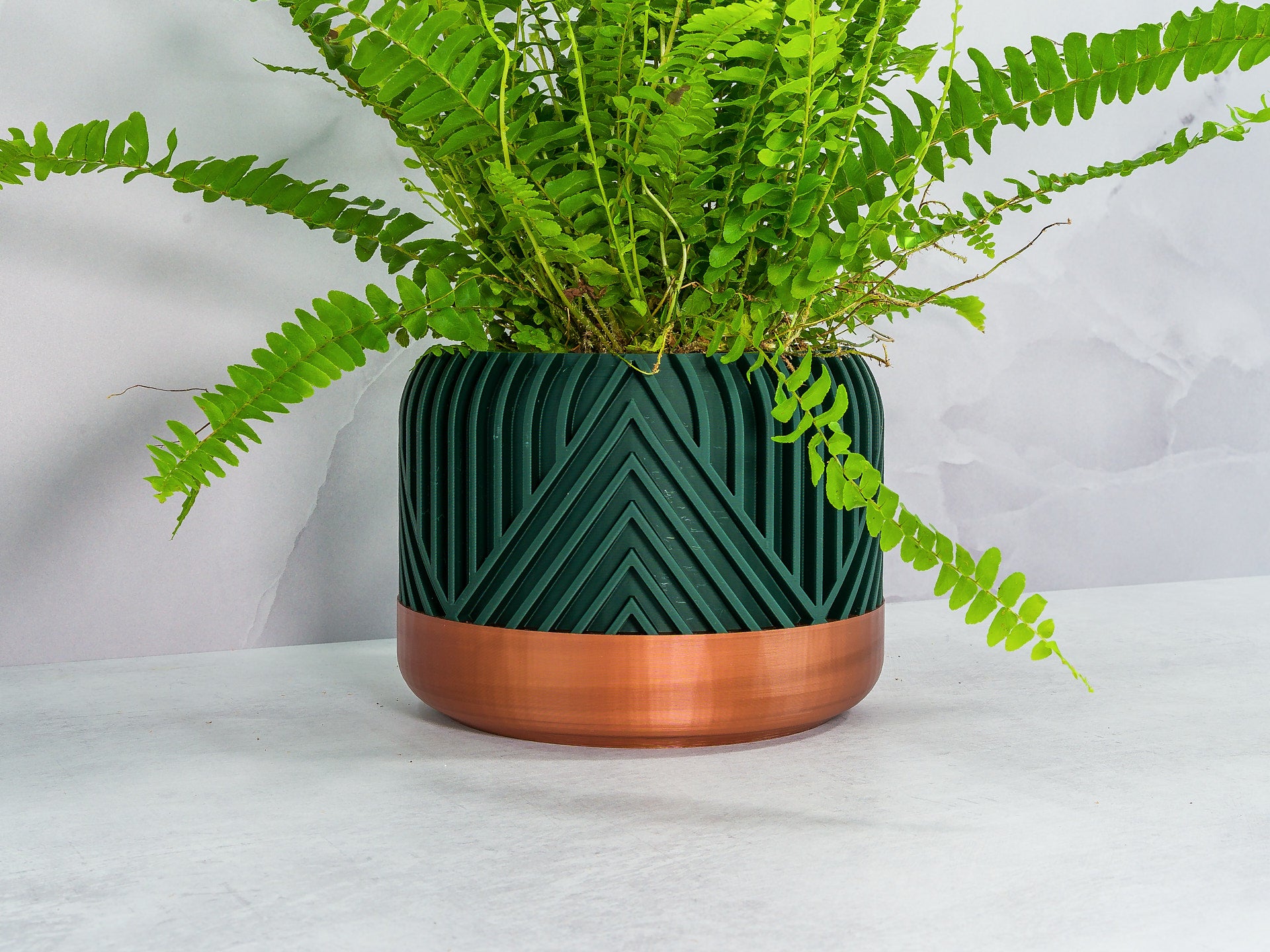 Angled with Fern: "Angled view of VERTI planter with copper base and forest pattern, showcasing a fern plant."
