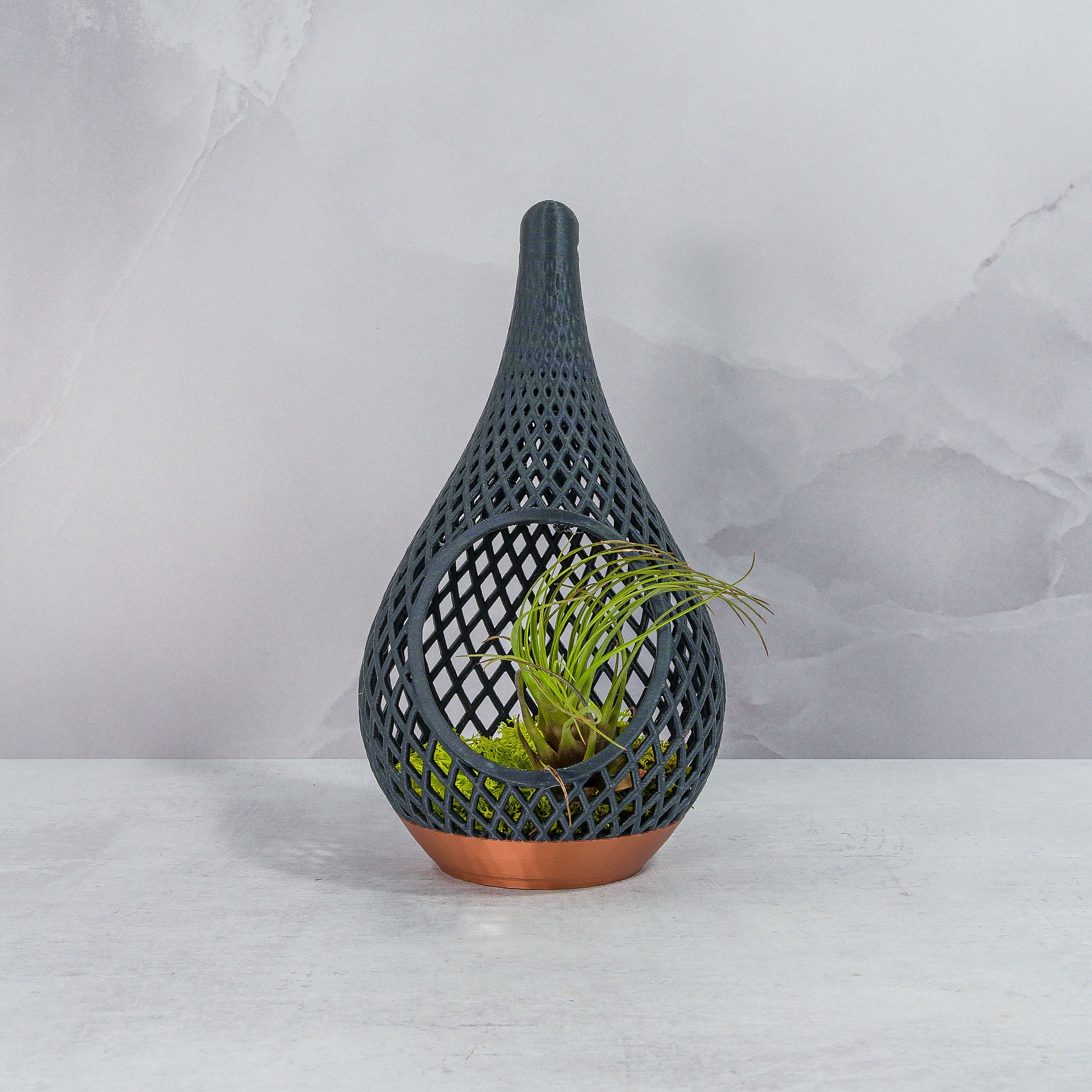 "Sitting, front-facing COPPER AND CARBON TEARDROP planter displayed with preserved moss and a delicate air plant, highlighting its modern aesthetic."
