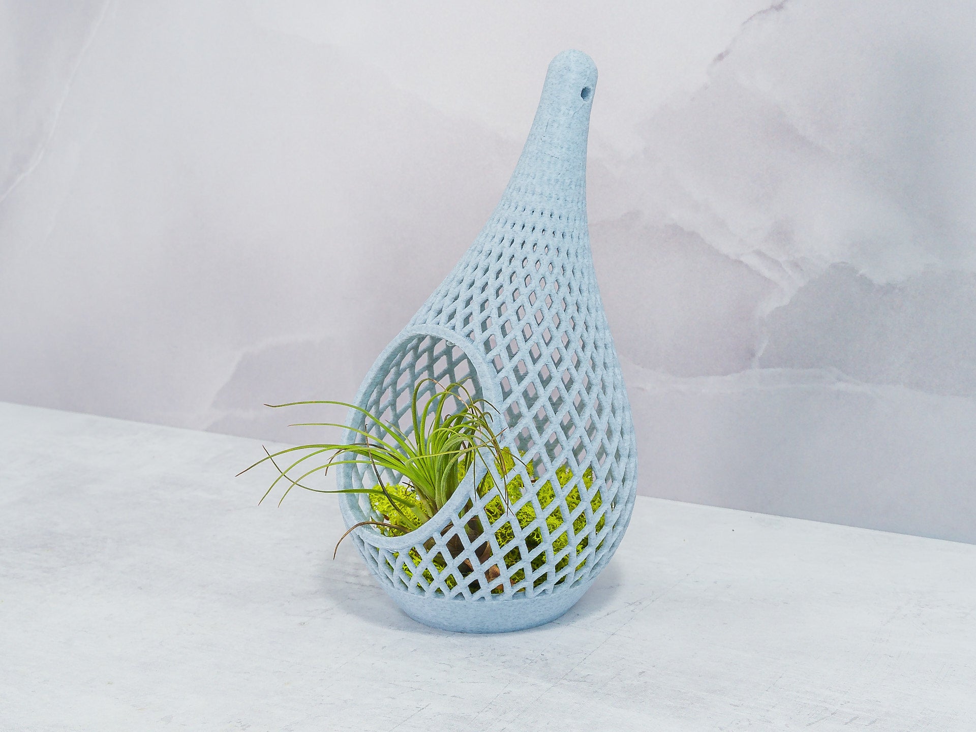 "Angled view of MARBLE TEARDROP planter sitting and showcasing preserved moss with an air plant, highlighting the unique marble textures."
