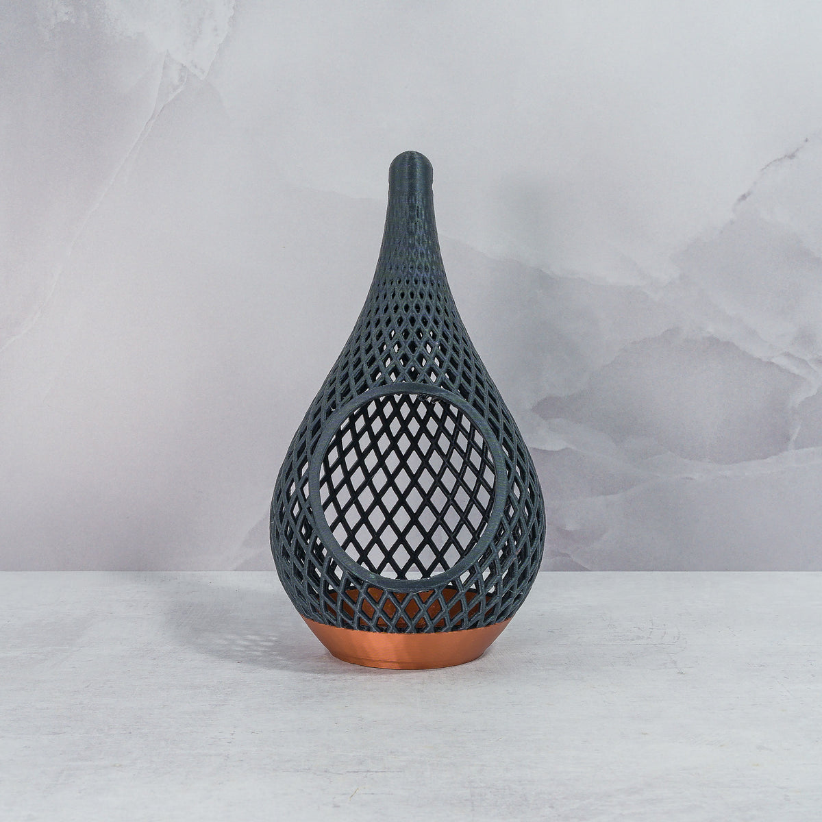 "Sitting, front-facing, empty COPPER AND CARBON TEARDROP planter, showcasing its striking design with a carbon fibre pattern."
